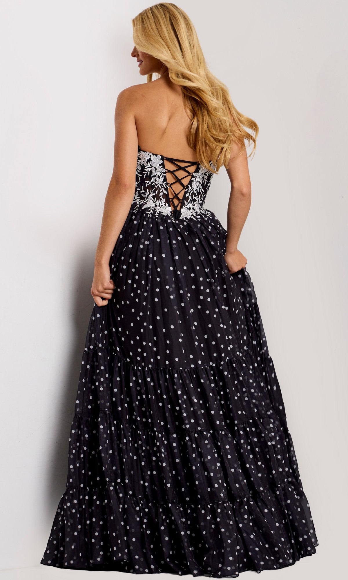 Woman wearing the Jovani 49086 long prom dress with a strapless floral lace corset bodice and A-line polka dot skirt, standing against a plain background.